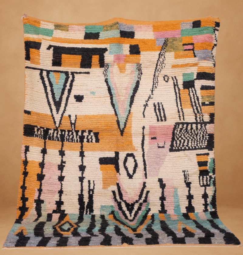 Boujad rug with an abstract, tribal-inspired design featuring bold black shapes and soft pastel tones of peach, mint, lavender, and mustard on a cream background. The handwoven wool texture adds depth to the intricate, symbolic patterns. Displayed vertically with subtle fringe, set against a warm neutral backdrop
