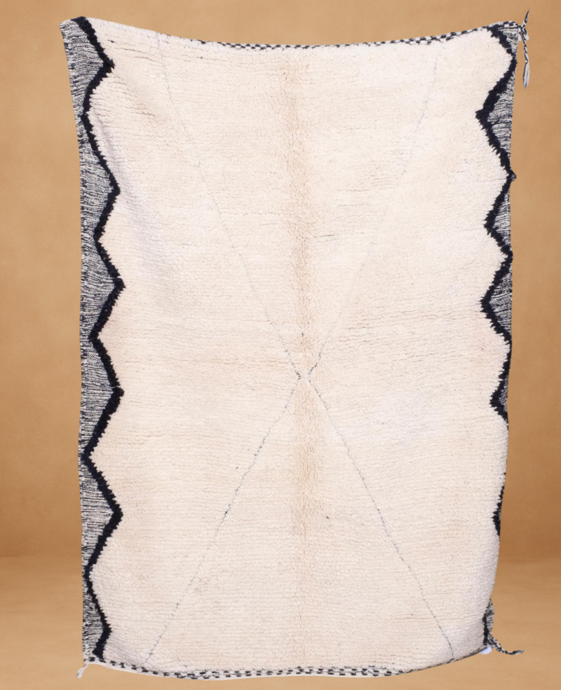 Beni Ouarain rug with a soft ivory wool base, featuring subtle linear detailing forming an X shape and bold black zigzag patterns along the left and right edges. Handwoven with a minimalist aesthetic, the rug is displayed vertically against a warm neutral background.