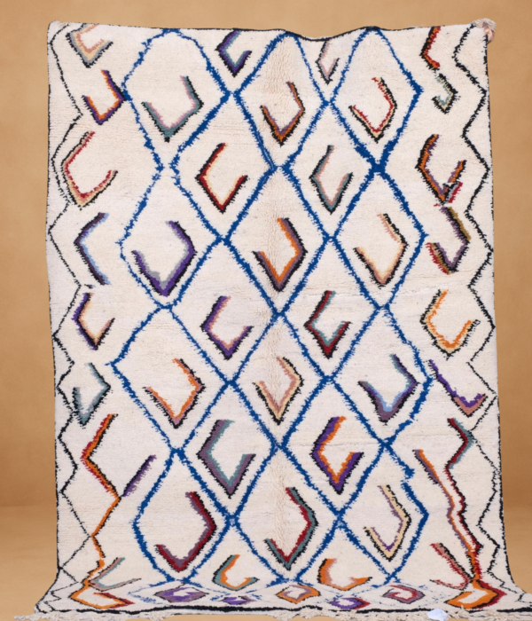 Beni Ouarain rug with a cream-colored wool base and a repeating diamond pattern outlined in blue, filled with multicolored V-shaped accents in shades of orange, purple, black, and red. The handwoven texture and vibrant geometry give it a lively yet traditional Berber feel. Displayed vertically with fringe along the bottom against a neutral background.